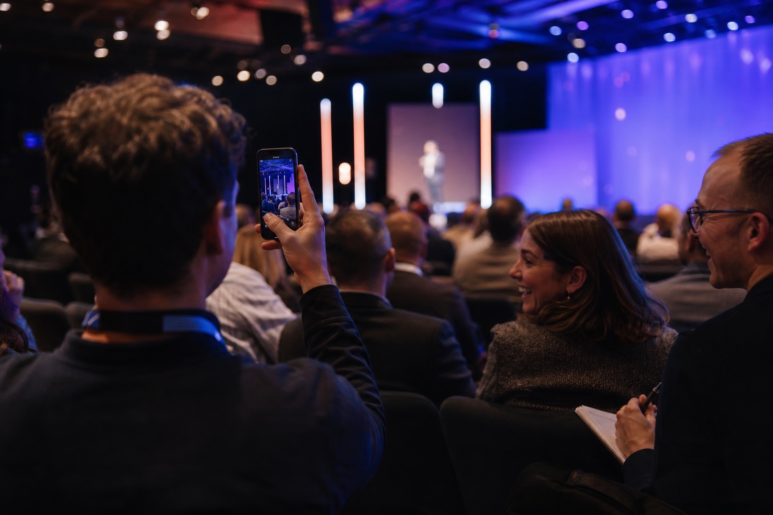 Conference attendee photographing a keynote while nearby attendees react